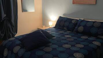A bedroom with a bed, a nightstand, a lamp, a wall-mounted air conditioner, and a framed picture.