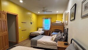 A room with two bunk beds, a wooden door, a ceiling fan, and a window with curtains. - Mountain View 3-bedroom apartment in Carrabassett Valley 10 minutes to Sugarloaf (Carrabassett Valley)