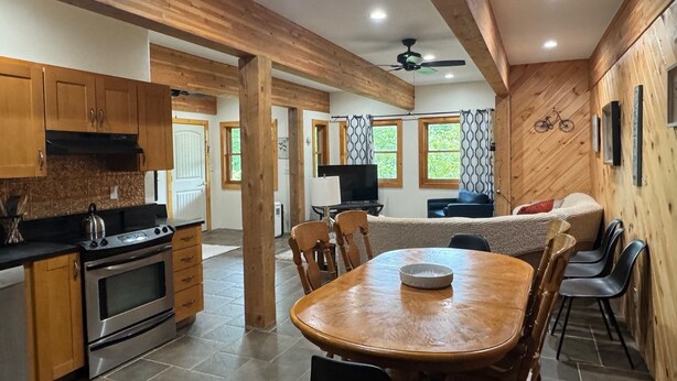A spacious kitchen with wooden beams, a dining area with a round table, and a living area with a sofa and TV. - Mountain View 3-bedroom apartment in Carrabassett Valley 10 minutes to Sugarloaf (Carrabassett Valley)