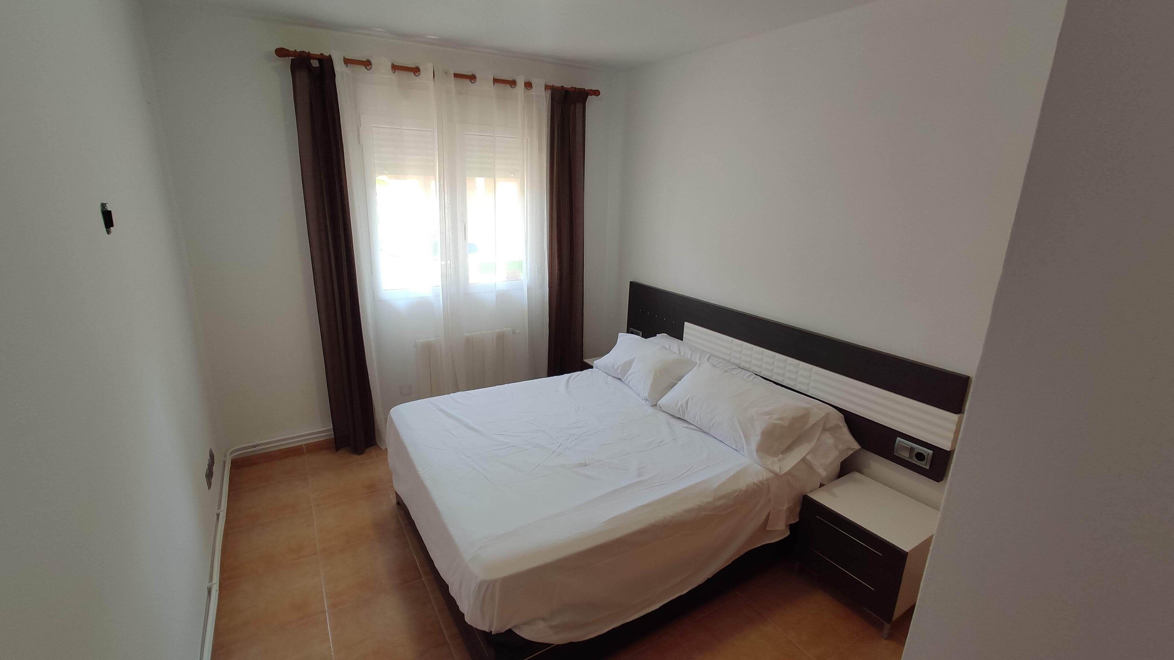 Una habitación de hotel con una cama individual, una mesita de noche y una ventana con cortinas.