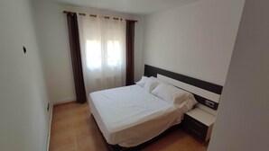 A hotel room with a single bed, a nightstand, and a window with curtains. - BENIVILLAGE (Benicarló)