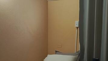 Una camera d'albergo con due letti singoli, una ventola a soffitto, un condizionatore d'aria, un comodino con una lampada e una finestra con tende.