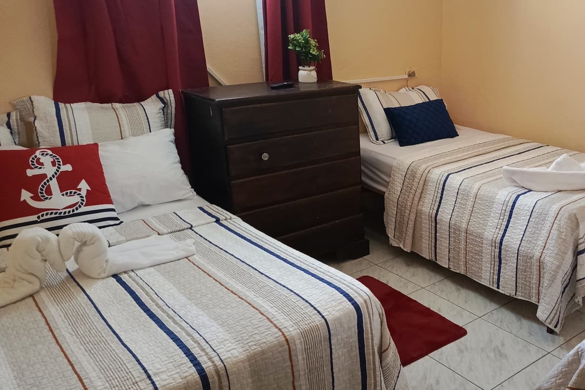 A hotel room with two single beds, a dresser, and a red curtain.