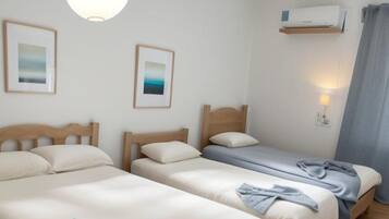 Habitación de hotel con dos camas individuales, una lámpara en el techo, un equipo de aire acondicionado y dos cuadros enmarcados en la pared.