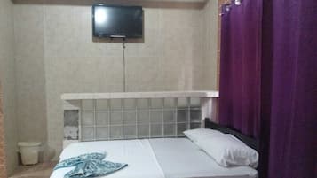 A bedroom with a bed, a television mounted on the wall, and a bathroom with a toilet and a trash bin.