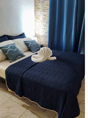 A bed with a navy blue quilt, a white seashell pillow, and matching pillows with blue wave patterns. - Pensión Galicia (David)