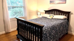 A bedroom with a wooden bed, a window with blinds, a bedside lamp, and a painting on the wall.