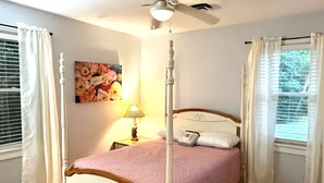 A four-poster bed with a headboard, a bedside table with a lamp, and a painting on the wall.
