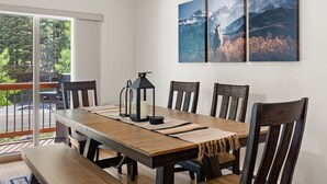 Un comedor con una mesa de madera, cuatro sillas, un farol y vistas a montañas a través de una ventana.