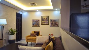 Una sala de estar moderna con un sofá, un sillón y un televisor de pantalla plana. Hay tres cuadros enmarcados en la pared y una planta en maceta.