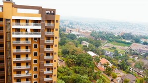 Un edificio de varios pisos con balcones, rodeado de vegetación y un paisaje urbano al fondo.