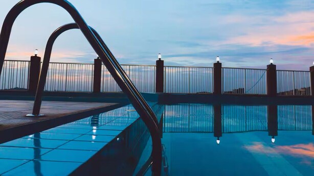 Una piscina con barandilla de metal y vista al atardecer sobre el agua.