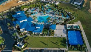 An aerial view of a resort with a central pool, multiple blue-roofed buildings, a basketball court, and surrounding greenery.