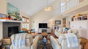 A spacious living room with a fireplace, comfortable seating, a television, and a balcony with a railing. - Relaxing Beachfront Escape (Galveston)