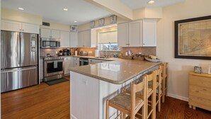 A modern kitchen with stainless steel appliances, white cabinetry, and a central island with bar stools. - Relaxing Beachfront Escape (Galveston)