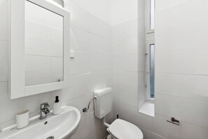 Un baño moderno con lavamanos, espejo e inodoro blancos.