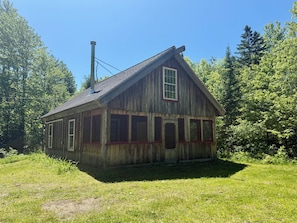 A wooden cabin with a gabled roof, surrounded by trees.