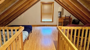 A small attic room with a sloped ceiling, wooden beams, a window with blinds, a desk with a chair, and two bunk beds. - Charming cabin with AC in Burnham - Perfect getaway. (Burnham)