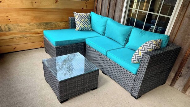 A sectional sofa with teal cushions and patterned pillows, a glass-top coffee table, and a concrete floor. - Charming cabin with AC in Burnham - Perfect getaway. (Burnham)