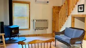 A cozy living room with a fireplace, a sofa, a wooden chair, and a staircase. - Charming cabin with AC in Burnham - Perfect getaway. (Burnham)