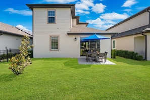 A two-story house with a patio area, a small tree, and a clear blue sky.
