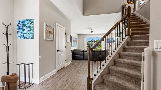 A spacious hallway with a wooden staircase, a black leather sofa, and a ceiling fan.