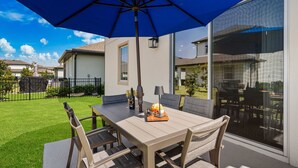 An outdoor patio with a table, chairs, a blue umbrella, and a glass door leading to a covered area.
