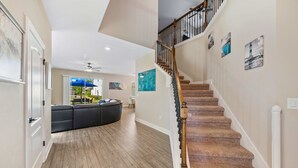 A spacious hallway with a curved black leather sofa, a wooden floor, and a carpeted staircase with a railing.