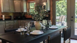 Une table à manger dressée avec des assiettes, des verres et des couverts, dans un intérieur en bois agrémenté de meubles et offrant une vue sur l’extérieur.