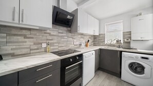 Eine moderne Küche mit Einbauofen, Geschirrspüler und Mikrowelle. Sie verfügt über graue Schränke, eine Marmorarbeitsplatte und eine geflieste Spritzschutzwand.