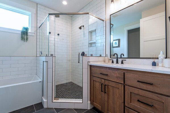 A modern bathroom with a glass-enclosed shower, a bathtub, wooden cabinets, and a large mirror.
