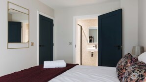 A hotel room with a bed, a large mirror, a door, a bathroom with a sink, and a nightstand with a lamp. - Experience a sense of deep calm with seaside walks & blissful sea air (Portrush)