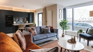 A modern living room with a grey sofa, a coffee table, and a view of the city through large windows. - Experience a sense of deep calm with seaside walks & blissful sea air (Portrush)