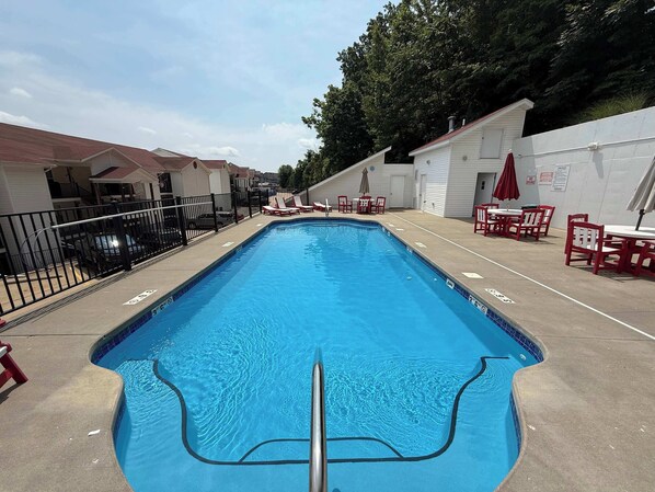 A rectangular swimming pool with a metal ladder in the center, surrounded by a concrete deck.