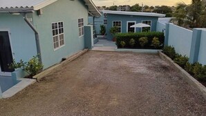 A residential area with a blue house, a gravel driveway, and a small garden with a palm tree. - Casa Di Meche – Apartment (Sint Michiel)