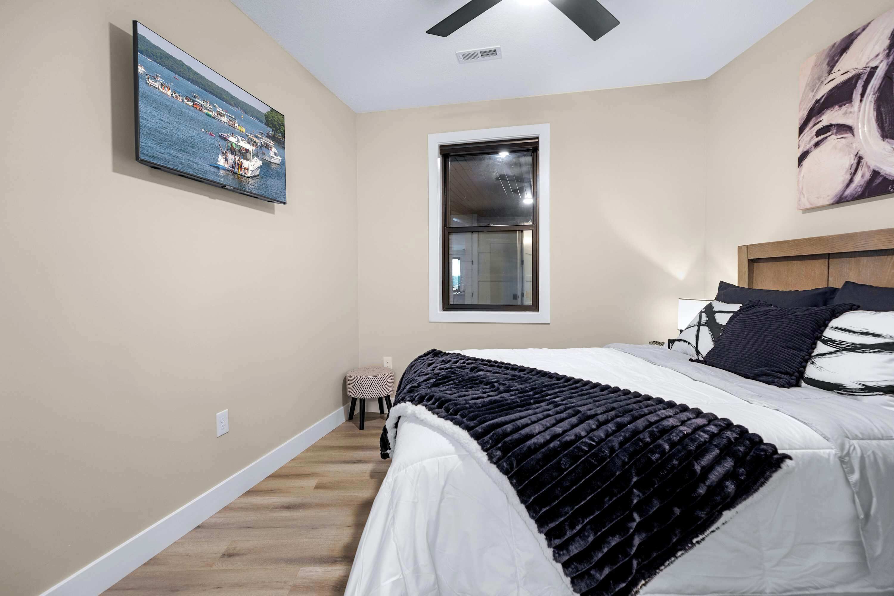 A bedroom with a bed, a window, a ceiling fan, and a painting on the wall.
