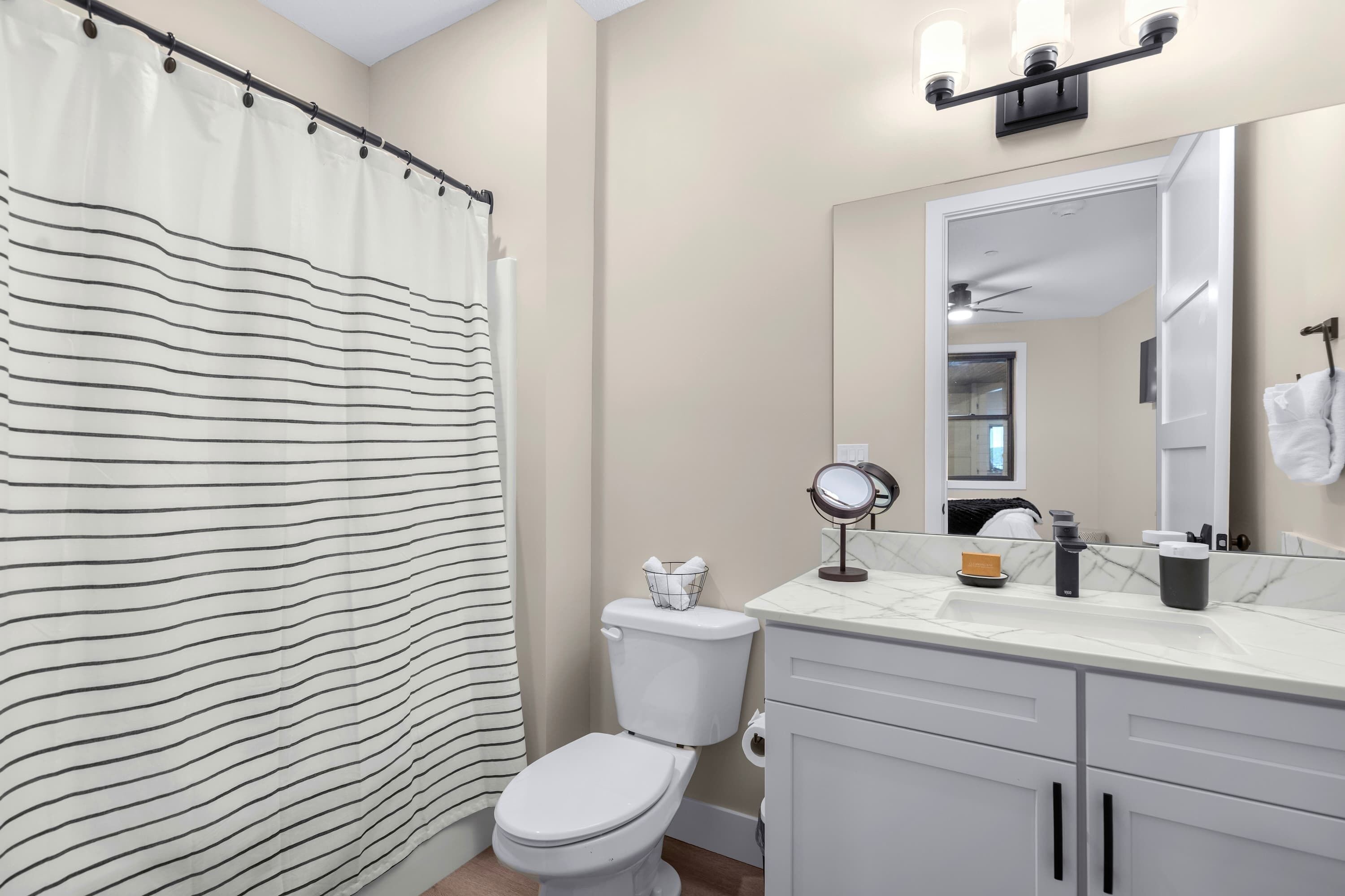A bathroom with a striped shower curtain, a toilet, a sink with a mirror, and cabinets.