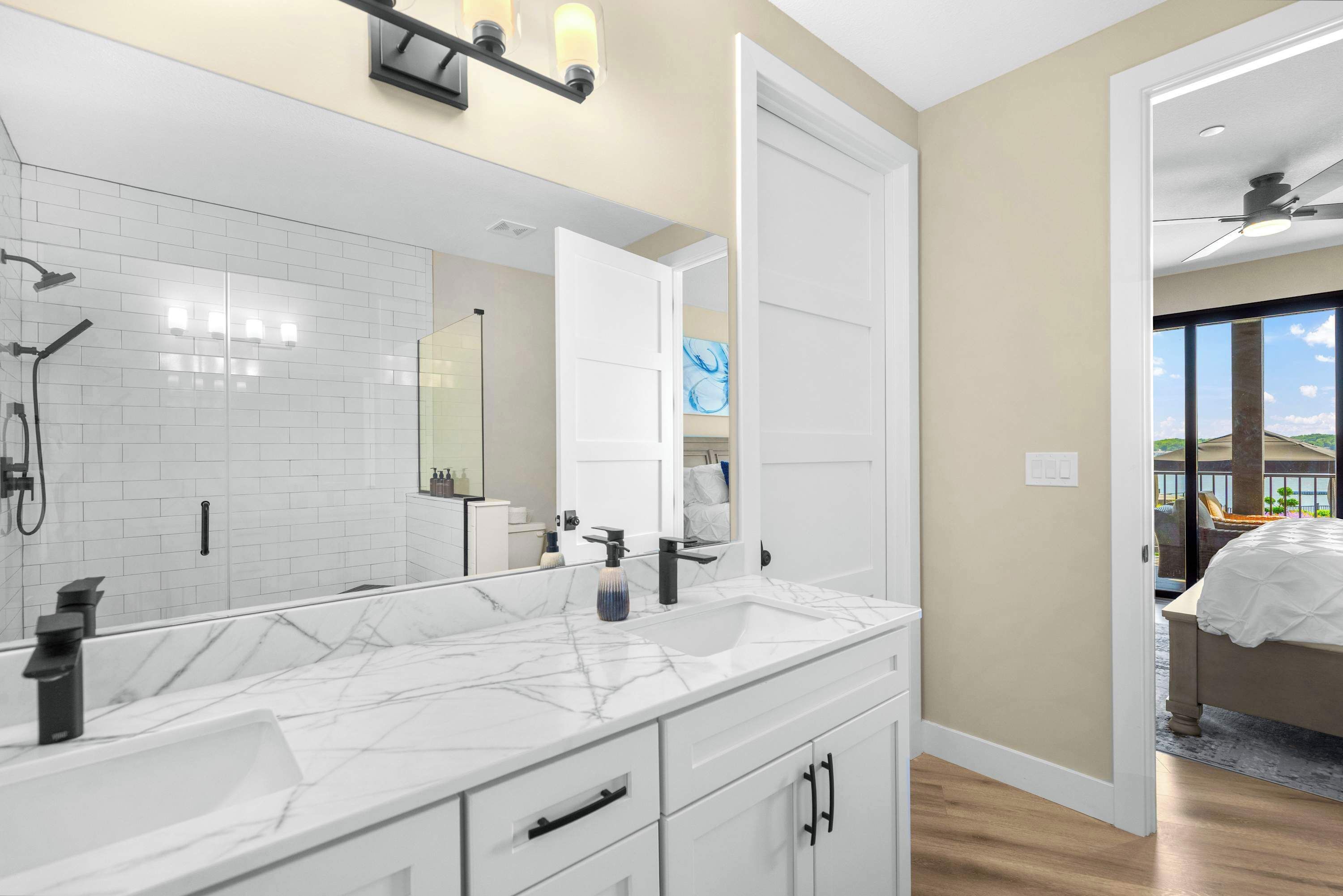 A modern bathroom with a large mirror, white marble countertop, and a shower with a handheld showerhead.