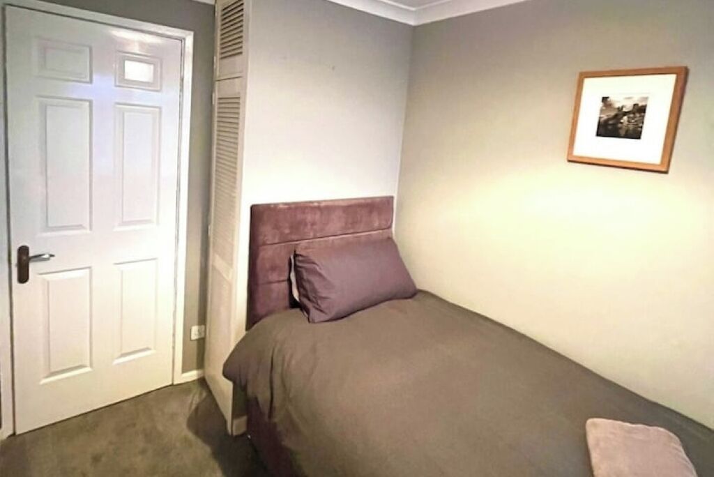 A bedroom with a single bed, a door, and a framed picture on the wall.