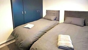 Ein Zimmer mit zwei Einzelbetten, einem dunkelblauen Schrank und einem kleinen Tisch mit einem Handtuch.