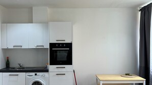 Una cocina moderna con armarios blancos, lavadora, una mesa con bancos y un cubo para fregar.