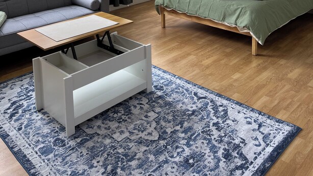 Un dormitorio moderno con un sofá gris, una cama con ropa de cama verde, un armario blanco y una alfombra azul estampada.