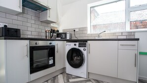 Une cuisine compacte équipée d’un lave-linge, d’un four, d’un four à micro-ondes et d’une fenêtre donnant sur un immeuble en briques.