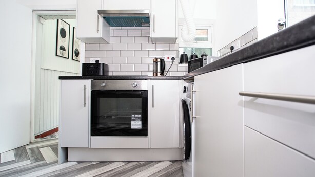 Une cuisine moderne avec des meubles blancs, un parquet à motifs en chevrons et des appareils électroménagers en acier inoxydable.