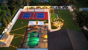 Vue aérienne d’une cour arrière comprenant un court de tennis, une piscine et un espace barbecue.