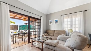 A living room with a sofa, a glass coffee table, and a dining area with chairs and a table.