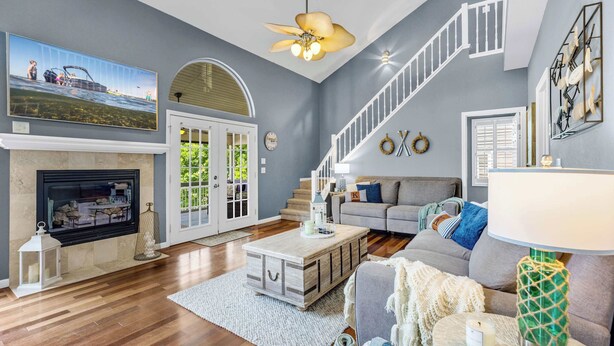 A spacious living room with a fireplace, a staircase, and a large window overlooking a garden. - Shore Thing - Lakefront for 12 (Lake Ozark)