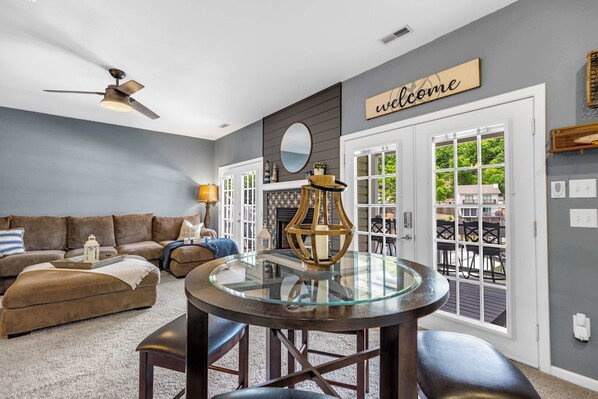A living room with a glass-top table, a ceiling fan, a sofa, and a 'welcome' sign. - Shore Thing - Lakefront for 12 (Lake Ozark)