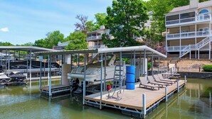 A marina with docked boats, a covered boat lift, and a wooden dock with lounge chairs. - Shore Thing - Lakefront for 12 (Lake Ozark)