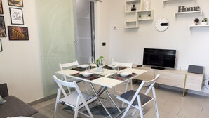Un salon moderne avec une table à manger, des chaises blanches, un canapé, un téléviseur et un ordinateur portable posé sur un bureau.